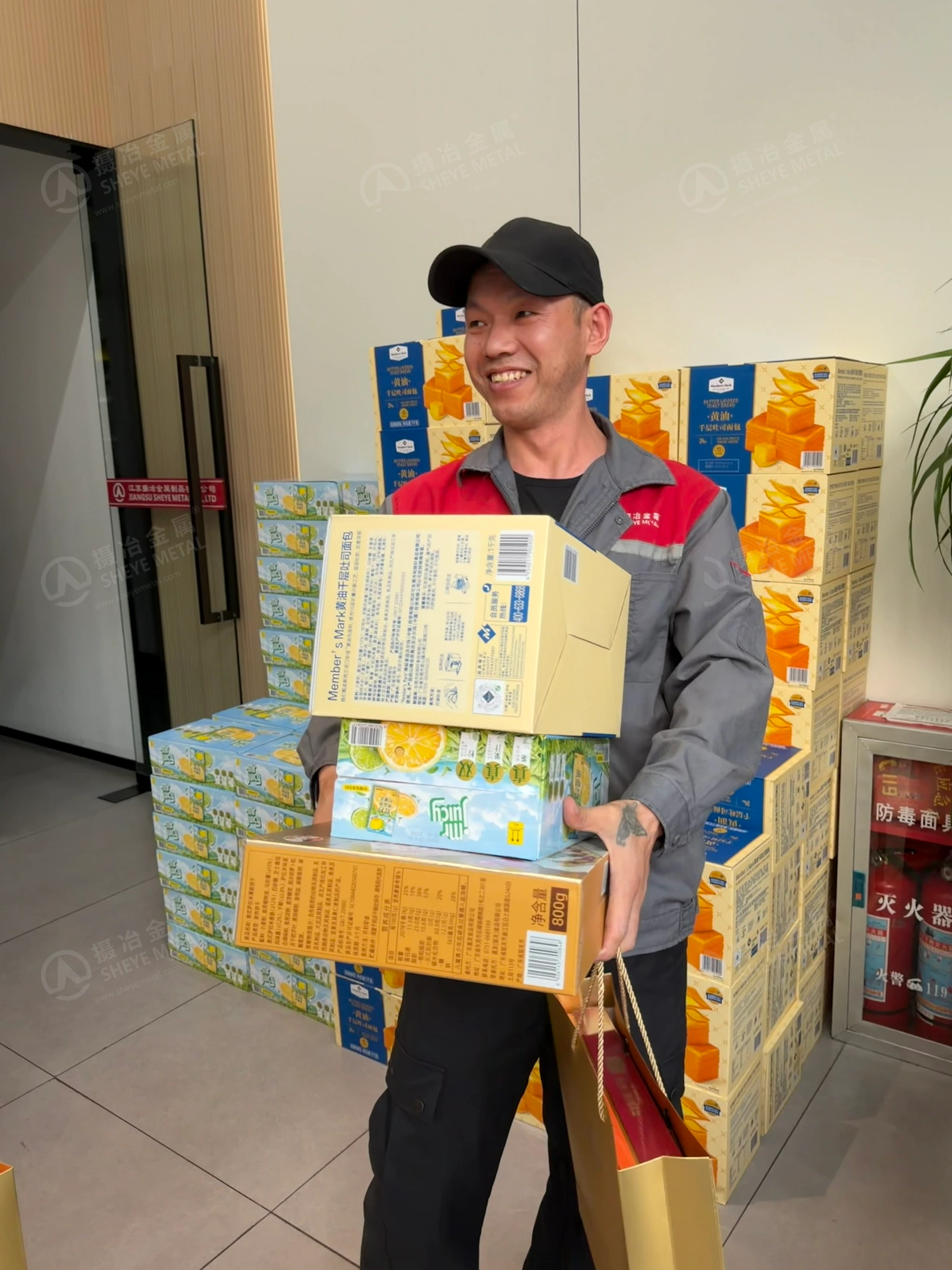 A smiling Sheye Metal colleague carrying food and drink gifts and a golden gift bag.