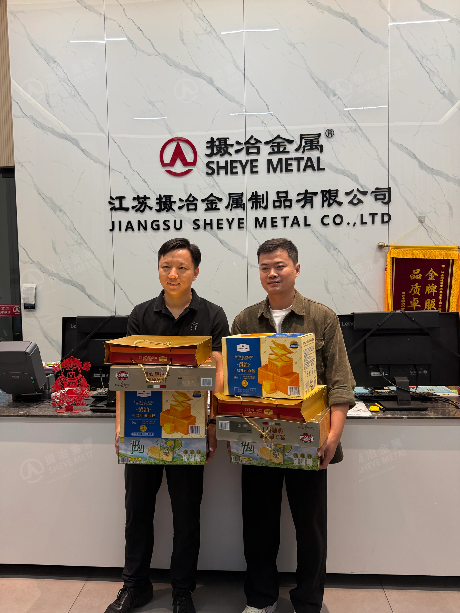 Two Sheye Metal colleagues holding holiday gifts beneath the company sign.
