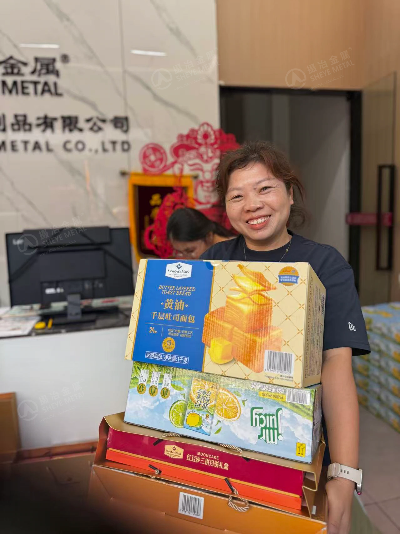 A smiling Sheye Metal colleague holding mooncakes, baked treats and drinks.